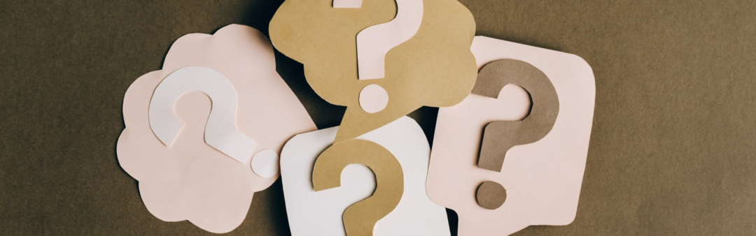 Papier-Fragezeichen in verschiedenen Farben auf braunem Hintergrund.