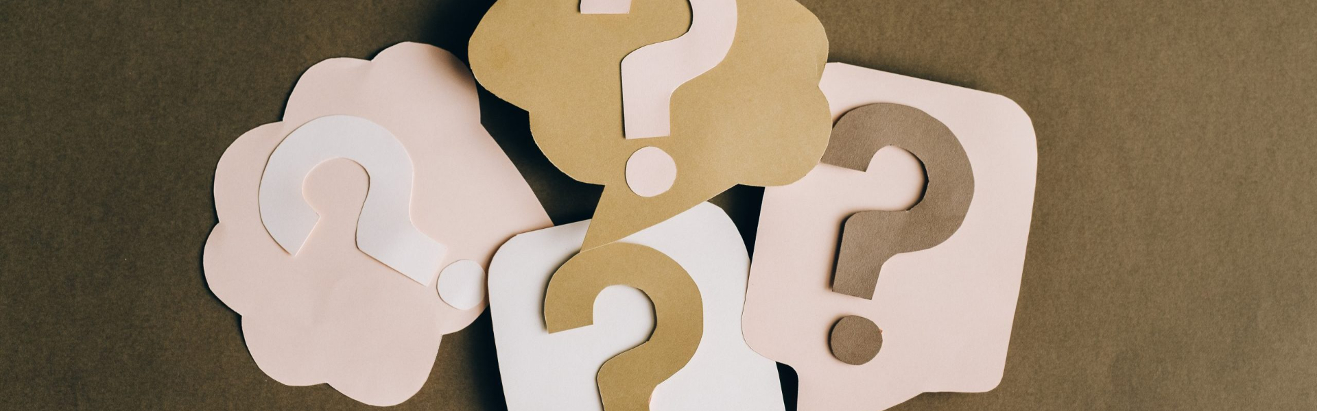 Papier-Fragezeichen in verschiedenen Farben auf braunem Hintergrund.