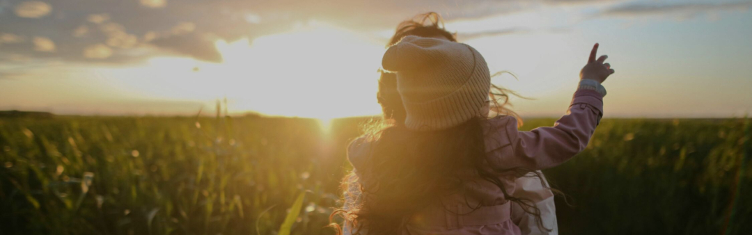 Kind zeigt auf Sonnenuntergang über Feld.